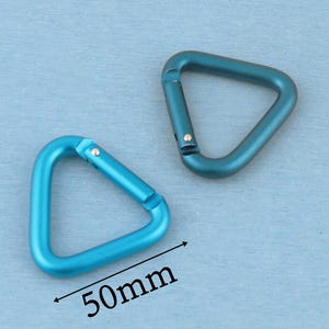 May include: Two triangular carabiners made of metal with a smooth finish. One carabiner is a bright sky blue, and the other is a darker teal blue. A black arrow and the text 50mm are printed below the sky blue carabiner to indicate its size.