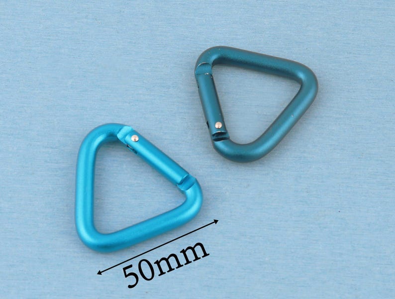 May include: Two triangular carabiners made of metal with a smooth finish. One carabiner is a bright sky blue, and the other is a darker teal blue. A black arrow and the text 50mm are printed below the sky blue carabiner to indicate its size.