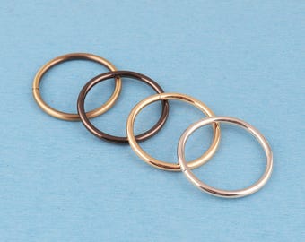 Può includere: Un set di quattro anelli circolari in varie finiture metalliche, tra cui oro, oro rosa, marrone scuro e bronzo. Ogni anello presenta un design liscio e senza giunture con un profilo sottile e arrotondato, disposti in una linea diagonale.