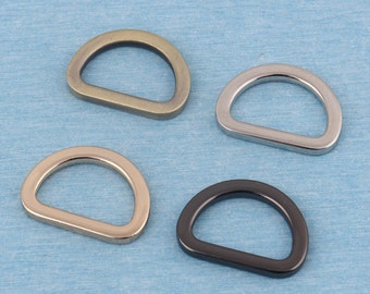 May include: Four metal D-rings in different finishes: antique brass, silver, nickel, and black. The rings are all the same size and shape.