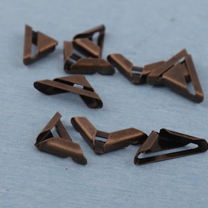 Op de afbeelding: Een verzameling antiek bronzen metalen fotohouders. Deze kleine, driehoekige stukken hebben een gevouwen ontwerp met een sleuf voor het vasthouden van foto's. Ze zijn verspreid op een lichtblauwe ondergrond.