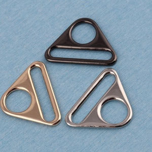May include: Three triangle-shaped metal slider buckles in black, gold, and silver.