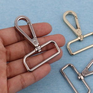 Op de afbeelding: Drie zilveren metalen draaibare sluitingen met rechthoekige lussen. De sluitingen bevinden zich in verschillende posities op een hand.