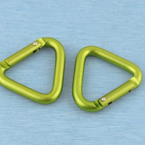 May include: Two lime green triangular carabiners with a smooth metallic finish. Each carabiner features a spring-loaded gate mechanism that allows for opening and closing, constructed from a single piece of lightweight metal shaped into a triangle.