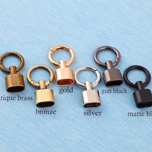 Könnte beinhalten: Metall-Drehhaken in verschiedenen Ausführungen: Antik-Messing, Bronze, Gold, Silber, Gun-Black und Matt-Schwarz. Jeder Haken hat einen Ring und eine rechteckige Basis, ideal für Bastelarbeiten und Accessoires.