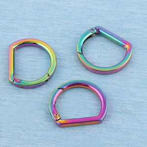 Peut inclure: Trois anneaux métalliques en forme de D avec une finition arc-en-ciel irisée vibrante. Chaque anneau comprend un mécanisme de fermeture à ressort articulé, permettant à la boucle de s'ouvrir et de se fermer pour diverses fixations.