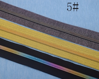 Puede incluir: Se muestran cuatro cintas de cremallera diferentes, incluyendo negro, dorado y gris, sobre un fondo azul. El texto "5#" es visible en la esquina superior derecha de la imagen.