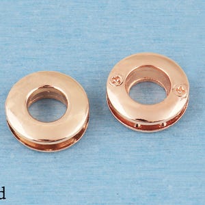 May include: Two circular gold-toned metal grommets with a smooth, polished finish. Each grommet features a central opening and a flat, ring-shaped design. The right grommet displays two small, visible screw heads on its surface. The word Gold is printed.