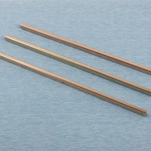 Pode incluir: Três varas de metal dourado de comprimentos diferentes. As varas são lisas e têm uma borda ligeiramente arredondada.