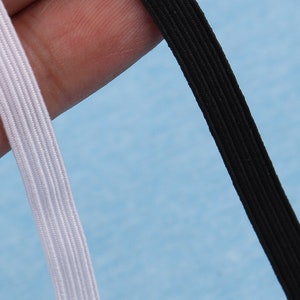 May include: Close-up of two pieces of elastic. One is white, the other is black. Both are ribbed and appear to be made of a woven material. The background is a light blue.