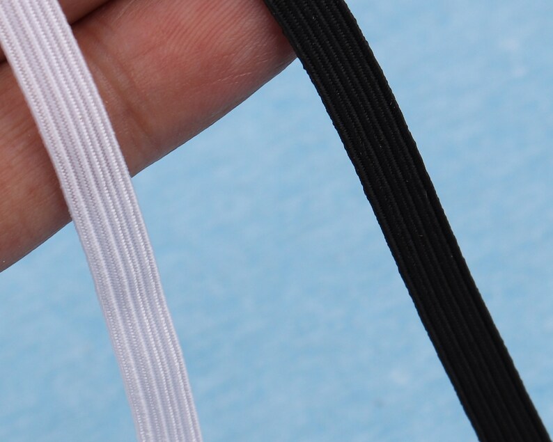 May include: Close-up of two pieces of elastic. One is white, the other is black. Both are ribbed and appear to be made of a woven material. The background is a light blue.