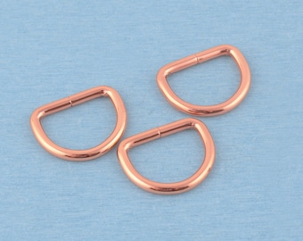 May include: Three polished rose gold metal D-rings with a smooth, rounded finish. Each piece features a classic semi-circular shape with a flat base and a curved top, showcasing a metallic sheen and a consistent, uniform rose gold color throughout.