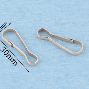 May include: Two silver-toned metal lobster claw clasps with a teardrop-shaped loop. The clasps are shown with dimension lines indicating a width of 10mm and a length of 30mm. The metal has a smooth, reflective finish and a simple, functional design.