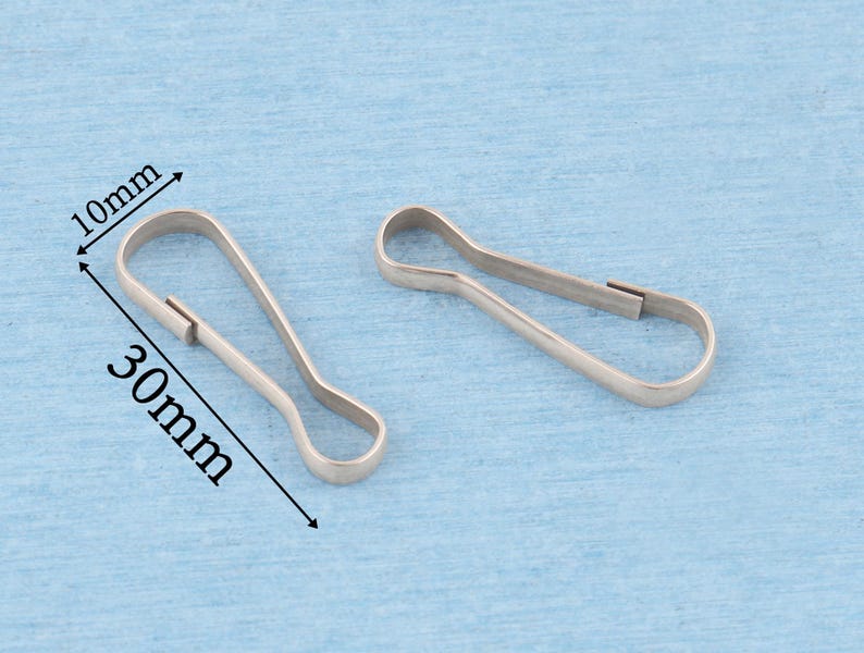 May include: Two silver-toned metal lobster claw clasps with a teardrop-shaped loop. The clasps are shown with dimension lines indicating a width of 10mm and a length of 30mm. The metal has a smooth, reflective finish and a simple, functional design.