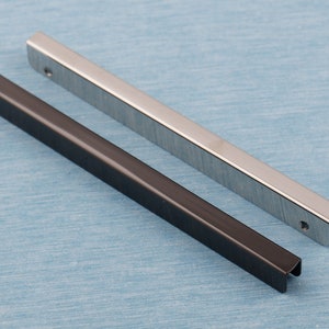 May include: Two metal handles, one black and one silver, are shown on a blue background. Both handles are rectangular in shape and have a slightly rounded edge.