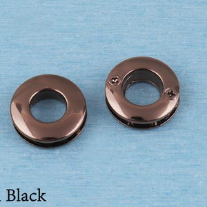 May include: Two circular metal grommets with a polished gun black finish. The grommet on the right features two small visible screws on its surface, while the grommet on the left is smooth. The text Gun Black is printed in the bottom left corner.