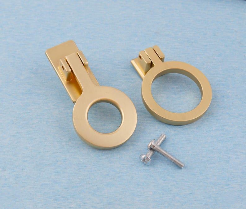 Puede incluir: Dos tiradores dorados para armarios con dise&ntilde;o circular y placa trasera rectangular. Se incluye un tornillo peque&ntilde;o. Los tiradores son de metal y est&aacute;n sobre un fondo azul claro. Adecuados para la restauraci&oacute;n de muebles o nuevas construcciones.