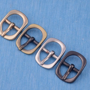 Peut inclure: Quatre boucles de ceinture métalliques dans différentes finitions : or, laiton, argent et noir. Les boucles sont toutes de la même taille et de la même forme, avec un cadre rectangulaire et une ouverture ronde.