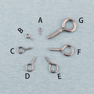 May include: A collection of seven silver-toned metal screw eyes labeled A through G, arranged in a circular pattern. Each screw eye features a circular loop at one end and a threaded screw shank at the other, varying in size from smallest to largest.