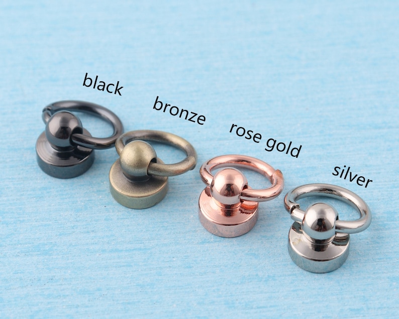 K&ouml;nnte beinhalten: F&uuml;nf Metallringe mit einer Kugel oben, in Schwarz, Bronze, Ros&eacute;gold und Silber.