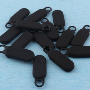 Może przedstawiać: Stosik czarnych suwaków do zamków błyskawicznych z metalową pętlą na górze. Suwaki do zamków błyskawicznych są wykonane z miękkiego, elastycznego materiału.