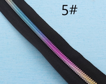 Puede incluir: Primer plano de una cremallera negra con un tirador de cremallera metálico de color arcoíris. La cremallera está etiquetada con "5#" en la esquina superior derecha de la imagen.