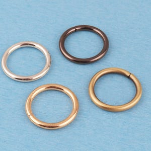 May include: Four circular rings arranged in a cluster, featuring distinct metallic finishes including a bright silver tone, a dark brown or black tone, a warm yellow gold tone, and a soft rose gold tone, each with a seamless, smooth, continuous band.