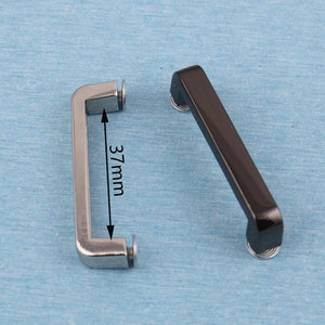 May include: Two metal handles, one silver and one black, with a measurement of 37 mm. The handles are designed for attaching to bags or other items.