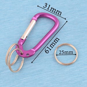 May include: A purple carabiner with a silver spring-loaded gate and two attached silver key rings. The carabiner measures 31mm in width and 61mm in length. A separate silver key ring with a 25mm diameter is positioned next to the carabiner.
