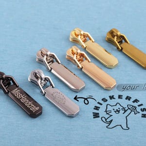 May include: Six metal zipper pulls in various metallic finishes including black, silver, rose gold, and gold. Each pull features a rectangular tab. One black pull is engraved with MissHandcraft, and one silver pull features a cat logo.