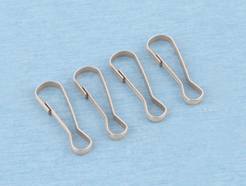 May include: Four silver-toned metal lanyard hooks, each featuring a teardrop-shaped loop at the bottom and a spring-loaded gate mechanism at the top, arranged in a diagonal row to display their uniform construction and metallic finish.