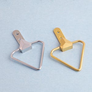 May include: Two metal cabinet pulls. One is silver, the other is gold. Each pull features a triangular handle and a rectangular base with a triangular accent. The pulls have a mounting plate with two holes.