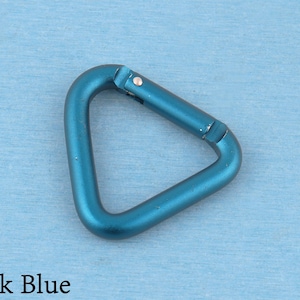 May include: A triangular carabiner with a metallic dark blue finish. The carabiner features a spring-loaded gate mechanism on one side, allowing it to open and close securely. The surface has a smooth, matte texture throughout the entire frame.