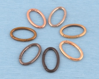 May include: A collection of seven oval-shaped metal spring gate rings arranged in a circular pattern. The rings feature various metallic finishes, including rose gold, polished gold, antique bronze, gunmetal, and matte black, each with a spring-loaded hinge.
