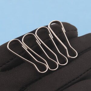 May include: Three silver-toned metal lobster claw clasps with a smooth, polished finish. Each clasp features a long, slender, teardrop-shaped loop design with a spring-loaded mechanism for secure attachment, arranged side by side.