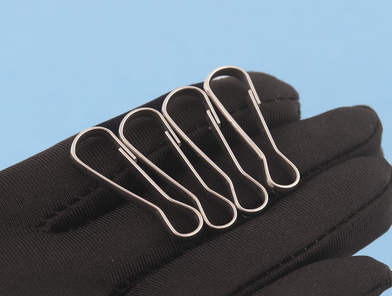 May include: Three silver-toned metal lobster claw clasps with a smooth, polished finish. Each clasp features a long, slender, teardrop-shaped loop design with a spring-loaded mechanism for secure attachment, arranged side by side.