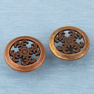 May include: Two decorative bronze-colored cabinet knobs. Each knob has a circular frame with an openwork floral design in the center. One knob has a darker, more reddish-brown finish, while the other has a lighter, golden-brown finish.