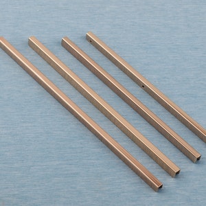 May include: Four metallic gold-colored metal strips with squared edges. The strips are arranged in a staggered pattern, with the longest strip at the bottom and the shortest strip at the top.