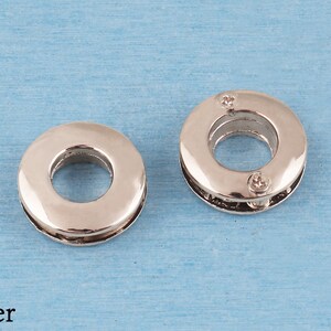 May include: Two circular silver-toned metal grommets with a smooth, reflective finish. Each grommet features a central opening and a two-piece construction held together by small screws visible on the surface of the right-hand piece.