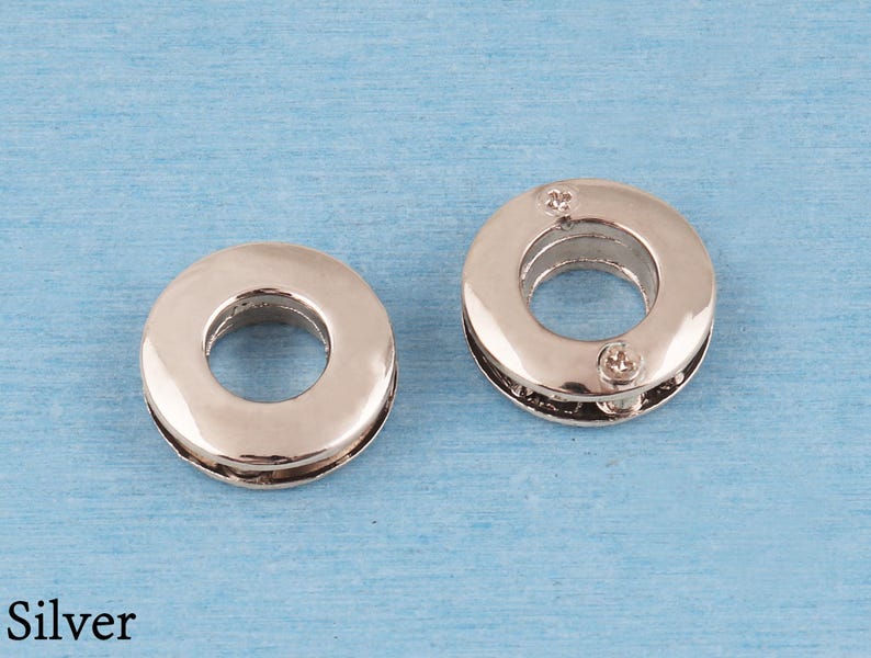 May include: Two circular silver-toned metal grommets with a smooth, reflective finish. Each grommet features a central opening and a two-piece construction held together by small screws visible on the surface of the right-hand piece.