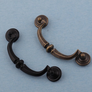 May include: Two decorative cabinet pulls. One is black, the other is bronze. Each pull has a curved handle and circular end pieces. The pulls are designed for easy installation on drawers or cabinet doors. These pulls add a vintage touch to furniture.