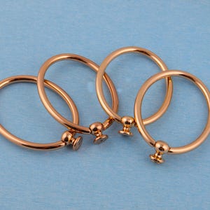 Könnte beinhalten: Vier Schubladengriffe aus roségoldfarbenem Metall. Jeder Griff hat ein kreisförmiges Design mit einem dekorativen Knopf. Sie liegen auf einer hellblauen Oberfläche. Durchmesser ca. 6 cm.