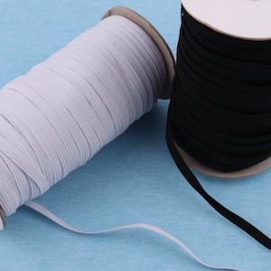 May include: Two spools of elastic ribbon, one white and one black, are displayed against a light blue background. The elastic is tightly wound around cardboard cores. The white elastic is unwound slightly, showing the flat, thin nature of the material.