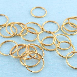 May include: A close-up of a group of gold-colored key rings on a light blue surface. The key rings are arranged in a random pattern.