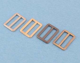 May include: Four rectangular metal strap adjusters arranged in a row. Each slider features a center bar and rounded corners. The finishes include light silver, bright gold, dark bronze, and a muted copper tone, all with a smooth metallic surface.