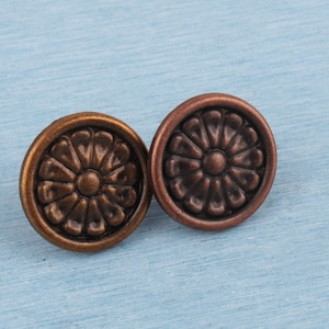 May include: Two antique bronze-colored cabinet knobs with a floral design. The knobs are round with a raised, detailed pattern resembling a flower. They are set against a light blue background.