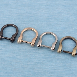 Könnte beinhalten: Vier D-Ringe aus Metall in verschiedenen Ausführungen: Schwarz, Gold, Silber und Antik-Messing. Die Ringe sind alle gleich groß und haben die gleiche Form, mit einer abgerundeten Öffnung und einem geraden Balken oben.