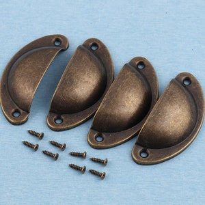 Puede incluir: Cuatro tiradores de armario de latón antiguo con forma redondeada de medio círculo. Los tiradores están dispuestos en un semicírculo con los extremos abiertos hacia afuera. Se incluyen ocho tornillos pequeños para la instalación.