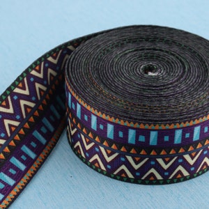 Puede incluir: Un rollo de cinta negra y naranja con un diseño geométrico. La cinta está tejida con una variedad de colores, incluyendo azul, verde y blanco.