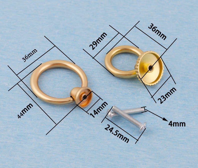 Op de afbeelding: Twee goudkleurige ringtrekkers met bevestigingsmateriaal. De ringtrekkers hebben een diameter van 3,6 cm en zijn 4,4 cm hoog. De ring zelf heeft een diameter van 2,9 cm. De basis heeft een diameter van 2,3 cm en is 1,4 cm hoog. Schroeven zijn 2,45 cm lang en 4 mm in diameter.